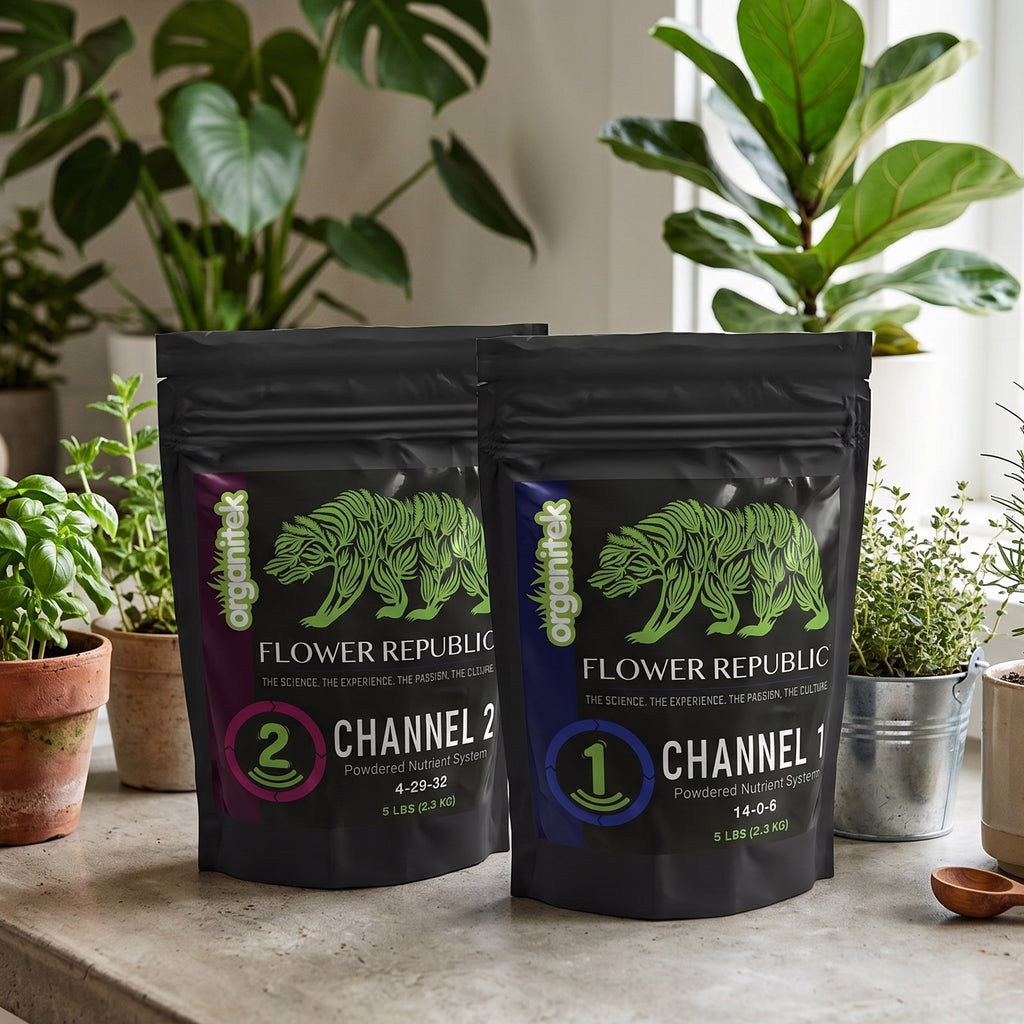 Two black stand-up pouches of Flower Republic plant nutrients, labeled Channel 1 and Channel 2, standing on a stone surface with potted plants in the background.